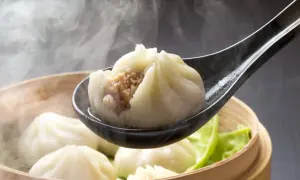 Gorące pierożki dim sum unoszą się w parze, jeden z nich na łyżce odsłania soczyste nadzienie.