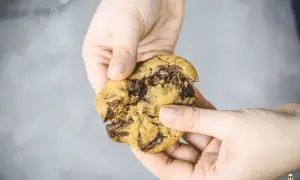 Hände halten einen frisch gebackenen Chocolate Chip Cookie, der nach einem einfachen cookie rezept gemacht wurde.