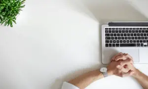 Dłonie splecione nad klawiaturą laptopa, obok zielona roślina. Może to być symbol trudnych decyzji, jak rozwód przez internet.