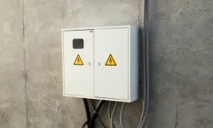 Biała skrzynka elektryczna z żółtymi symbolami ostrzegawczymi na betonowej ścianie. Zastanawiasz się, ile się czeka na podłączenie prądu do mieszkania?