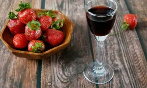 Aksamitna nalewka truskawkowa w kieliszku obok miseczki świeżych truskawek. Idealny deser na letnie wieczory.