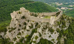 Vestiges d'un château abandonné en Occitanie, perché sur un éperon rocheux, dominant une vallée verdoyante.