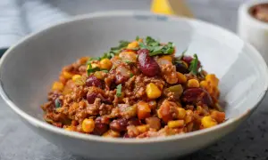 Miseczka pełna aromatycznego chili con carne z fasolą, kukurydzą i mielonym mięsem, posypana świeżą natką pietruszki.