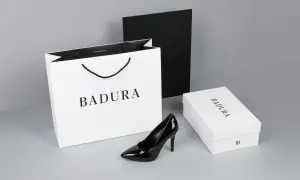 Elegancki czarny szpilka od firmy Badura, obok białej torby i pudełka z logo. Badura to polska marka obuwia.