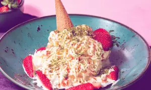 Spaghetti-Eis mit Erdbeeren und Pistazien in einer blauen Schale, garniert mit einer Eistüte.