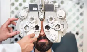 Optometrysta to specjalista od wzroku. Mężczyzna z brodą przechodzi badanie wzroku na foropterze.