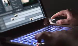 Dłoń steruje myszką przy laptopie z podświetlaną klawiaturą, edytując wideo w formacie HEVC.