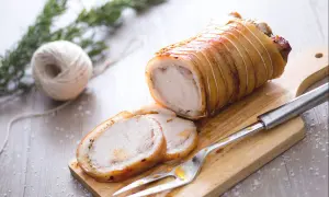 Ein aufgeschnittener, goldbraun gebratener Schweinebraten (Porchetta) auf einem Holzbrett mit Gabel und Rosmarin.