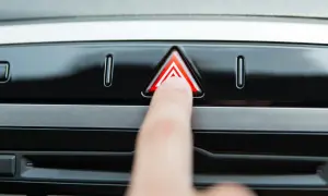 Un doigt appuie sur le bouton d'appel de feux stop, le triangle rouge s'illumine.