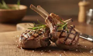 Costine allo spiedo succulente e grigliate, guarnite con rosmarino fresco e sale grosso su un tagliere di legno.