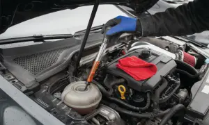 En hand med blå handske mäter glykol i bilen med en mätare. En röd trasa ligger på motorn.