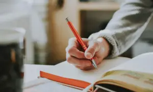 Mano escribiendo en un cuaderno con ejercicios de tiempos verbales en español.