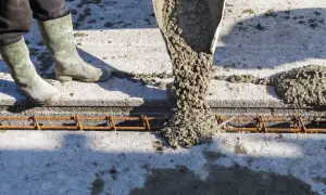 Beton wylewany z rury na zbrojenie. Pracownik w gumowcach stoi obok, nadzorując proces.