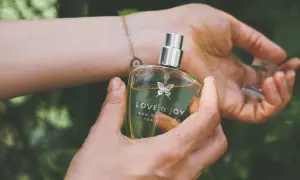 En hand håller en parfymflaska med texten "LOVE & JOY". Doften kan vara en fin present till en parfym gravid.