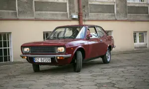 Czerwony fiat 128, klasyk z lat 70., zaparkowany na brukowanym dziedzińcu przed budynkiem.