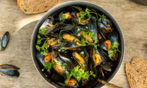 Un plat généreux de moules marinières, garni de persil frais, servi avec du pain de campagne sur une table en bois.