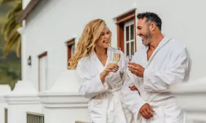 Para, ubrani w szlafroki, wznoszą toasty szampanem na balkonie. Zastanawiają się, ile kosztuje noc w hotelu, ciesząc się luksusem.