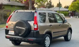 En gyllene Honda CRV 2005 står parkerad på en gata, med reservhjulet synligt på bakluckan.