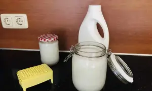 Zelf wasmiddel maken met dille en kamille. Glazen potten met wit wasmiddel, een gele rasp en een witte fles staan op het aanrecht.