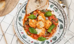 En tallrik med ricotta recept: smakliga ricotta-bollar i tomatsås med kikärtor, spenat och basilika, serverad med rostat bröd.