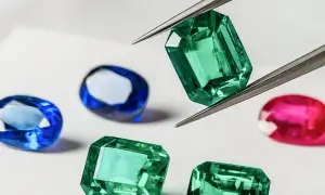 Pinzas sostienen una esmeralda verde brillante, rodeada de zafiros azules y un rubí rosa. Un tesoro de piedras preciosas.