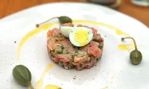 Un délicieux tartare de thon, garni d'un œuf de caille et de câpres, est servi sur une assiette blanche avec un filet d'huile d'olive.