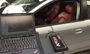 Laptop och KESS-enhet kopplade till en bil för att chippa bilen. Röd läderinredning syns i kupén.