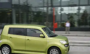 Zielony Daihatsu Materia jedzie ulicą obok nowoczesnego budynku.