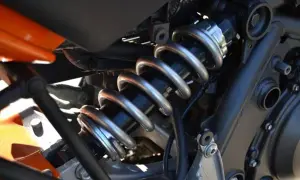 Gros plan sur l'amortisseur d'une moto, avec son ressort argenté et son corps noir. Une légère fuite d'amortisseur est visible, nécessitant une réparation.
