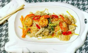 Deliziosi spaghetti di riso con gamberi succulenti e verdure croccanti, guarniti con semi di sesamo.