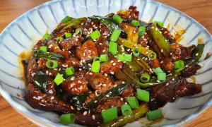 Un plat appétissant de boeuf aux oignons, garni de graines de sésame et d'oignons verts frais.
