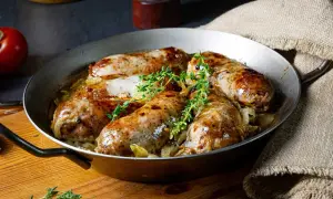 Pieczona w piekarniku biała kiełbasa surowa z cebulą i tymiankiem, podana w metalowej patelni.