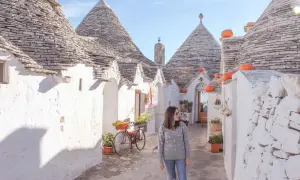 Una donna passeggia tra i trulli di Alberobello, un'icona di cosa vedere in Puglia. Le case coniche e i colori vivaci creano un'atmosfera magica.