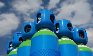 Butla z gazem do TIG spawania, niebiesko-zielona, pod błękitnym niebem z chmurami.