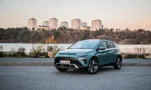 Grön Hyundai Bayon parkerad vid en sjö med stadssiluett i bakgrunden. En perfekt bil för en testkörning i skymningen.