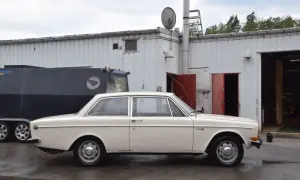 En vit Volvo 142 från 1973 står parkerad framför en industribyggnad.