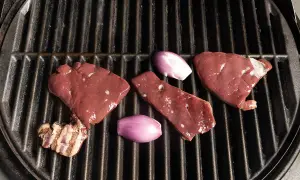 Rohe Leberstücke und Schalotten liegen bereit zum leber grillen auf einem heißen Rost.