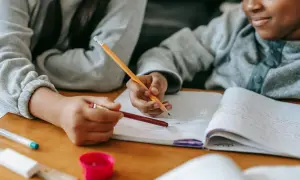 Dos niños concentrados en su dictado de 3 primaria, escribiendo en un cuaderno con lápices.