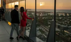 Para na tarasie Olivia Star podziwia zachód słońca nad miastem.