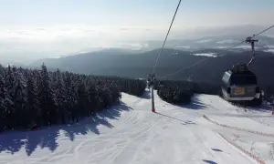 Trasa narciarska w Janskie Łaźnie, kolejka linowa wznosi się nad ośnieżonymi drzewami i stokiem.