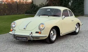 Klasyczny kremowy Porsche 356 z czerwoną tapicerką, zaparkowany na żwirowej nawierzchni.