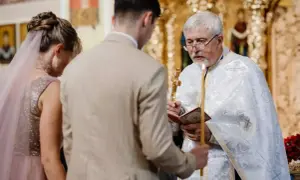 Para Młoda klęczy przed kapłanem podczas cichego ślubu kościelnego bez mszy. Kapłan trzyma krzyż i świecę.