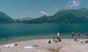 Ludzie odpoczywają na kamienistych plażach nad Jeziorem Como, ciesząc się słońcem i orzeźwiającą wodą.
