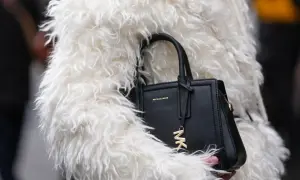 Czarna torebka Michael Kors z logo MK, otulona w białe futro. To marka znana z luksusowych akcesoriów.
