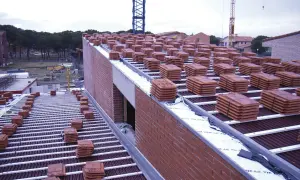 Pilotes de tejas rojas apiladas en la cubierta de una casa en construcción. Grúas en el fondo.