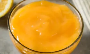 Gładki, żółty lemon curd w szklanej miseczce, obok połówka cytryny. Idealny do deserów.