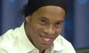 Uśmiechnięty Ronaldinho w białej koszuli i czarnej opasce na głowie, wspominający swoje najlepsze lata w różnych klubach.