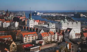 Widok na zamek i port w Szczecinie. Zabytkowe budowle z czerwonymi dachami kontrastują z błękitem wody i nieba.