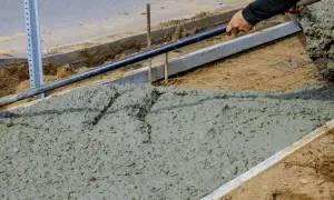 Prace budowlane: świeży beton, który będzie miał fakturę betonu szczotkowanego, jest rozkładany łopatą.