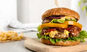 Soczysty burger z wołowiny z dodatkami na desce, obok frytki.